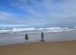 Two kids standing on the beach staring out at the sea