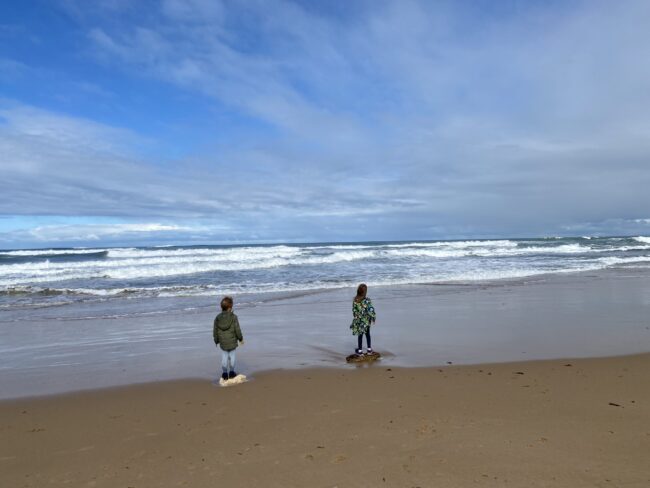 Two kids standing on the beach staring out at the sea
